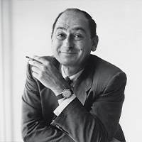 Zwart-wit portret van een man met een lachend gezicht. Hij zit casual in een pak, met een sigaret in zijn hand en een horloge om zijn pols.