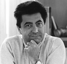 Black and white image of a man with short, straight hair. He rests his chin on his hand and has a relaxed but attentive expression.