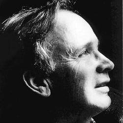 Fekete-fehér portré egy idős férfiról profilból. Reflexszerűen néz ki, és semleges háttér előtt egyszerű ingben van öltözve.