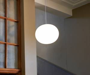 Weiße Glaskugel-Pendelleuchte mit sanftem Lichtschein im Treppenhaus