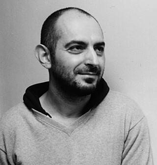 Retrato a preto e branco de um homem com cabelo curto e barba. Ele olha pensativamente para o lado, vestindo uma camisola informal.