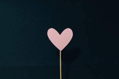 This image shows a simple pink heart on a stick with a black background