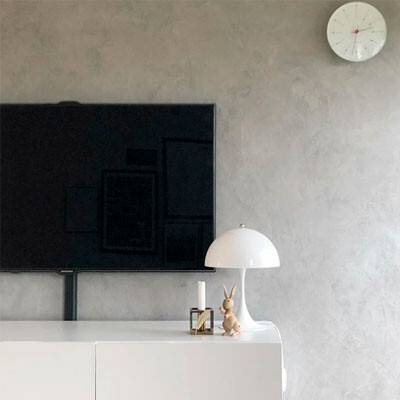 Esta imagem mostra um candeeiro de mesa Panthella Mini em branco sobre uma cómoda, em frente a um televisor