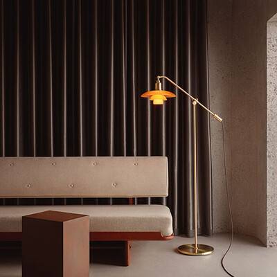 Dette billede viser en ravfarvet PH 3/2 Limited Edition gulvlampe, den står ved siden af en sofa