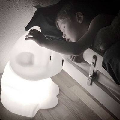 Esta imagem mostra um candeeiro infantil Nanuk com a forma de um urso e um rapaz a dormir agarrado a ele