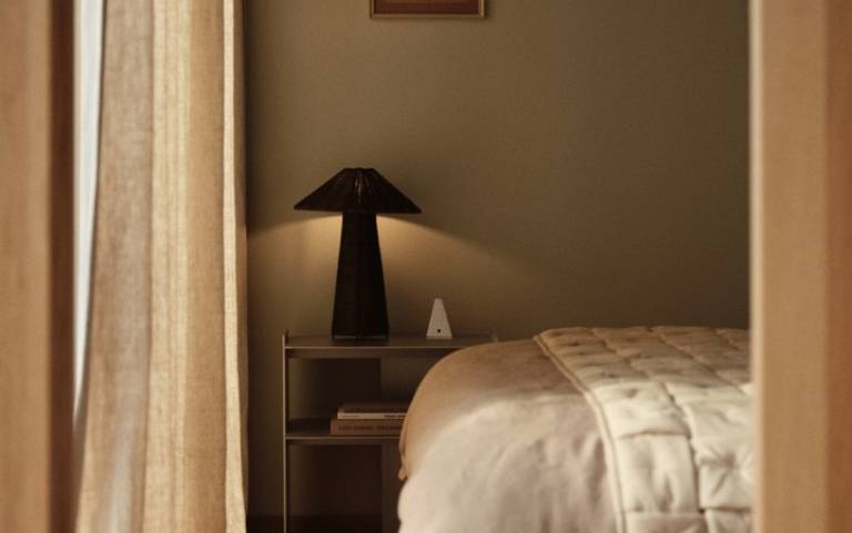 Lampa stołowa Dou z rattanu – dostępna w magazynie; stolik nocny obok łóżka z narzutą Sofi.