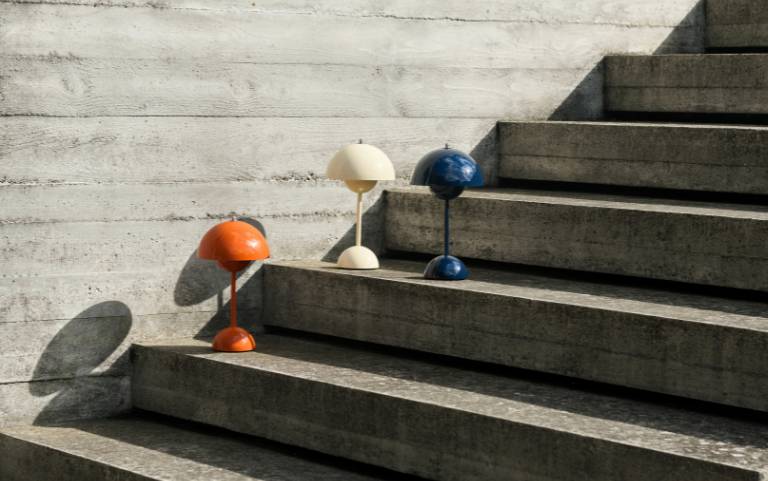 Tre lampade da tavolo &Tradition Flowerpot in blu, arancione e bianco crema si ergono su gradini di cemento alla luce del sole.