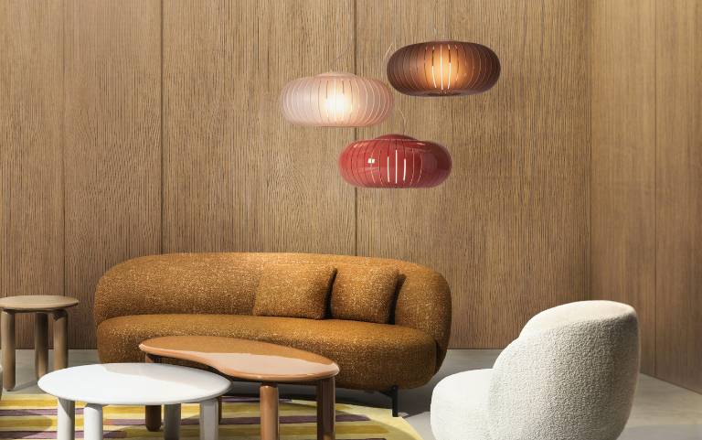 Skandinavisch inspiriertes Wohnzimmer mit warmen Holzflächen, weichen Lounge-Möbeln und gerippten Pendelleuchten in sanften Rot- und Naturtönen.