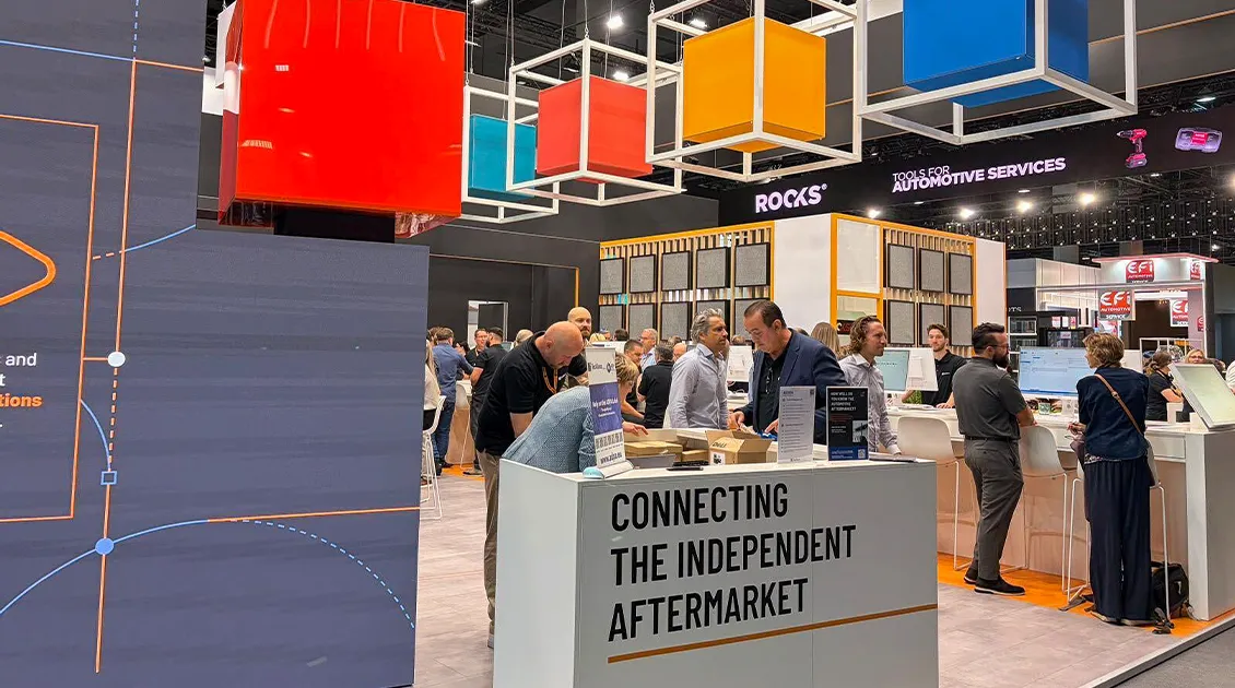 People interacting at a trade show booth with colorful cube displays above. A sign reads "Connecting the Independent Aftermarket."