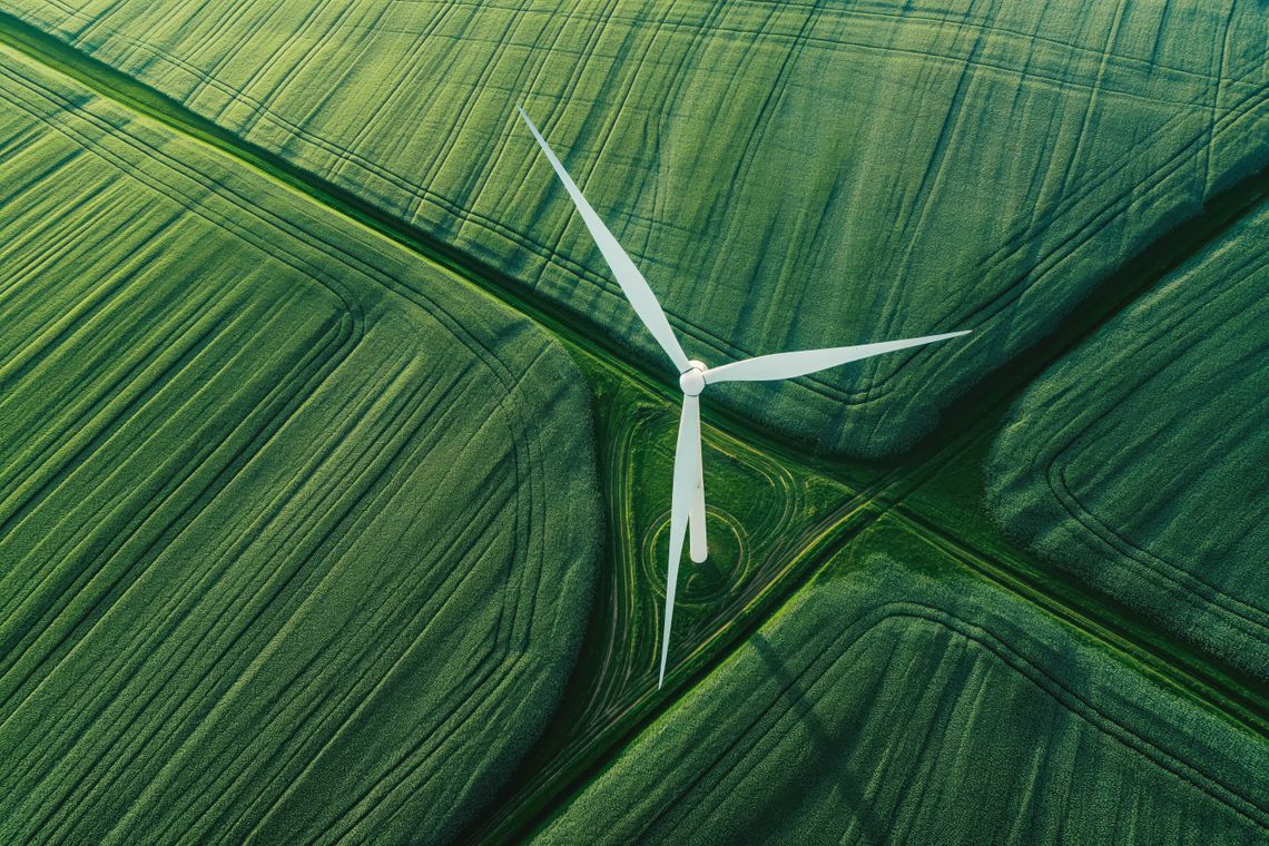 Aerial view of a wind turbine in the middle of green agricultural fields, symbolizing sustainability and responsible supply chain practices aligned with EUDR compliance.
