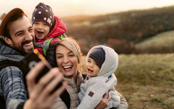 Eine Familie macht ein Selfie in der Natur, lacht und geniesst den Moment in einer herbstlichen Landschaft.