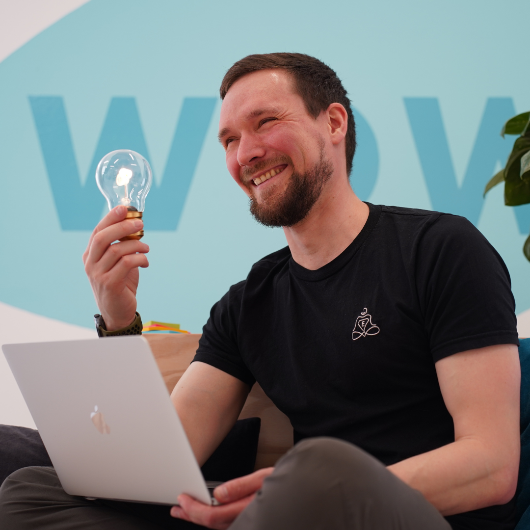 Johannes hält lächelnd Glühbirne - Entspannungshelden Gründer bei der Ideenfindung am Laptop