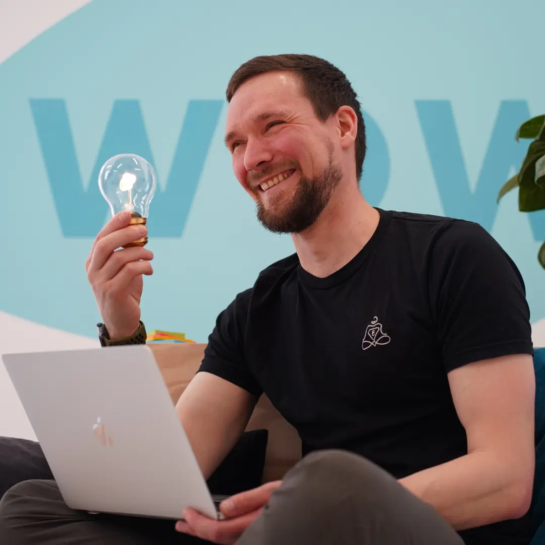 Johannes hält lächelnd Glühbirne - Entspannungshelden Gründer bei der Ideenfindung am Laptop
