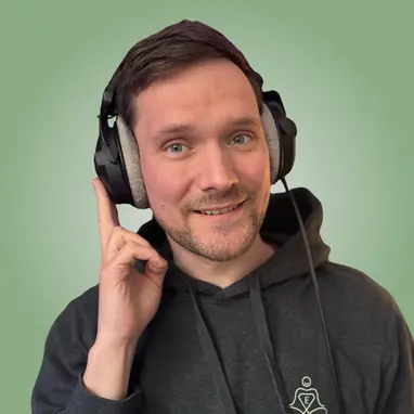 A person wearing a black hoodie and large headphones smiles and gestures with one hand against a green background.