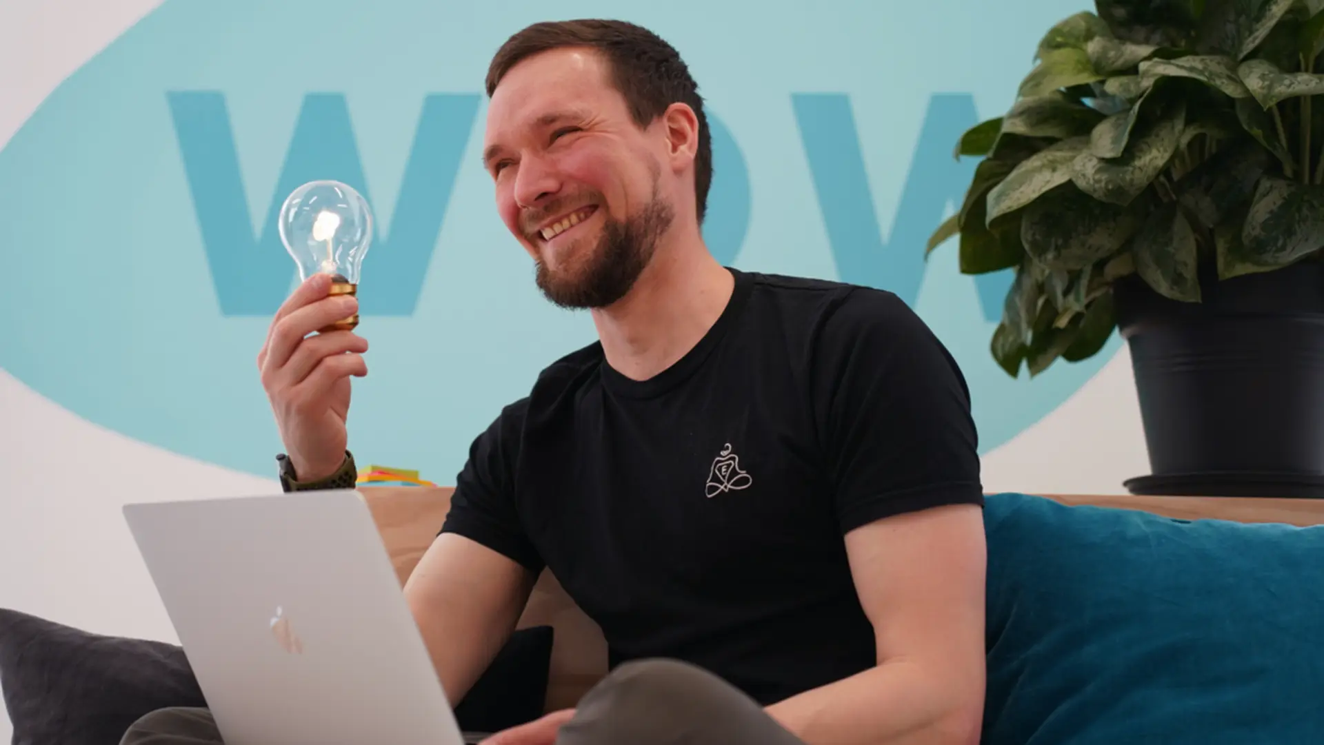 Johannes lächelnd mit Glühbirne am Laptop - kreativer Moment bei der Kursentwicklung