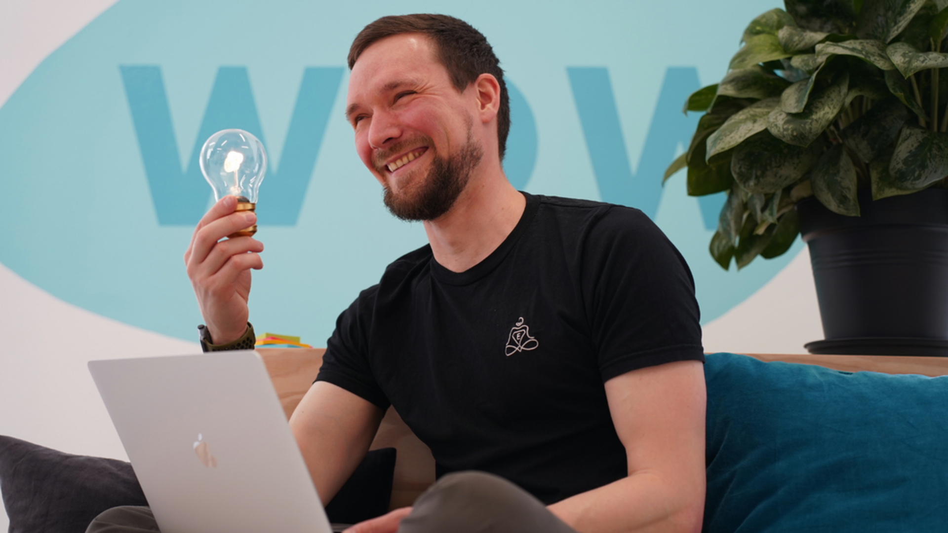 Johannes lächelnd mit Glühbirne am Laptop - kreativer Moment bei der Kursentwicklung