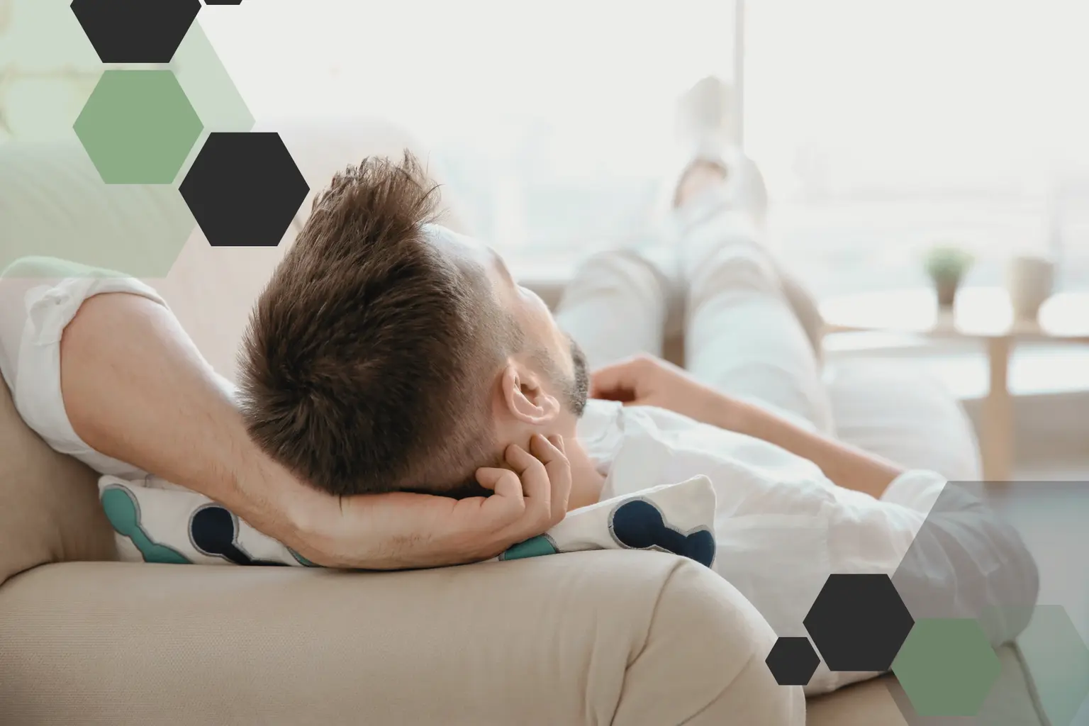 Man relaxing on a beige sofa with hands behind head, geometric hexagons overlay, bright and airy living room background.