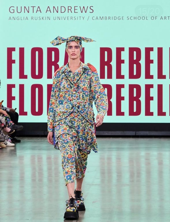 A female model on catwalk wearing blue, red, yellow mottled outfit with matching shoes and headscarf