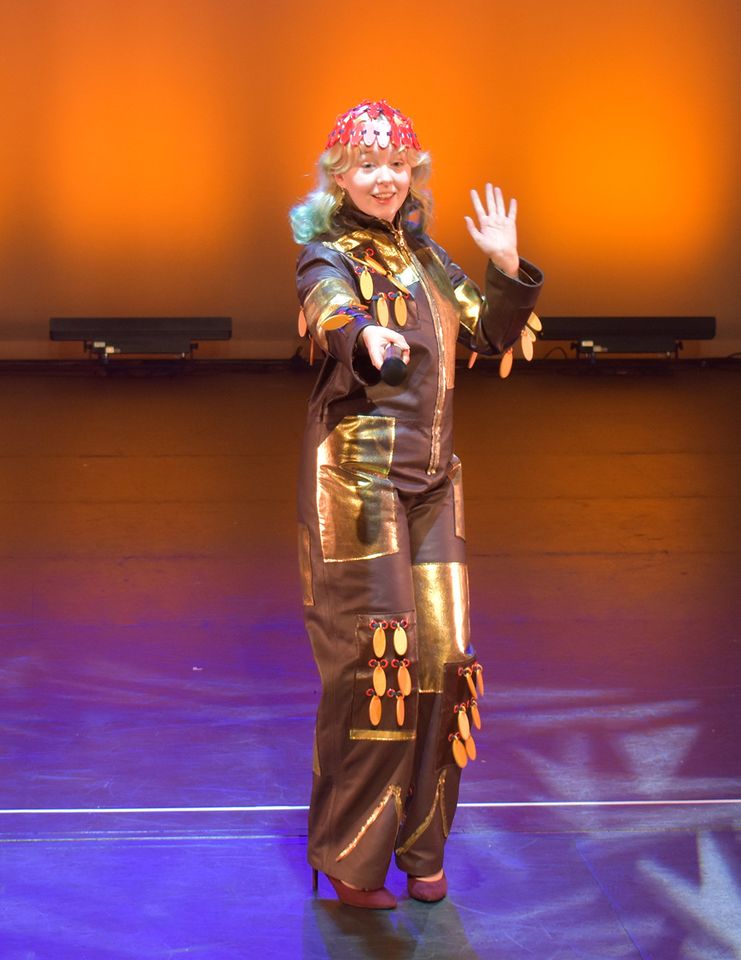 Photo of female model wearing brown and gold trouser suit and red head-dress