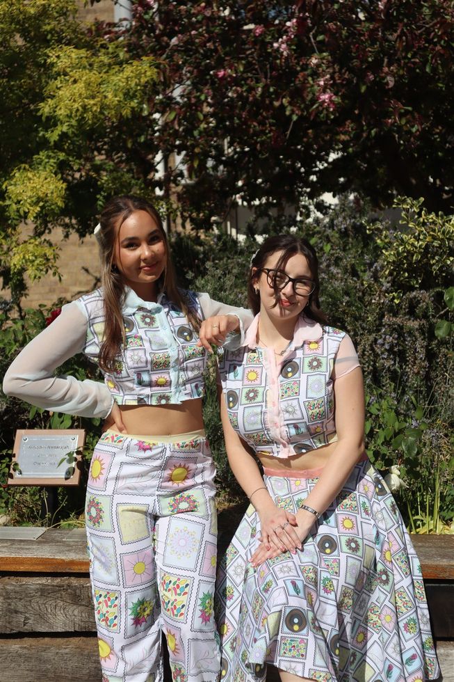 Two female models outside wearing white patterned trouser suit and dress