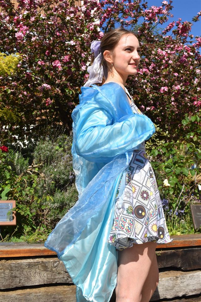 Female model outside wearing short white patterned dress with blue top