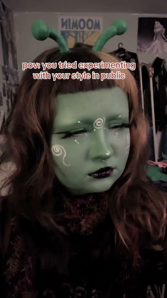 Young woman with green face paint and alien horns in room, subtitled "pov: you tried experimenting with your style in public"