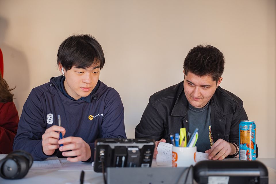 Photo of two men sat behind a desk watching small monitor