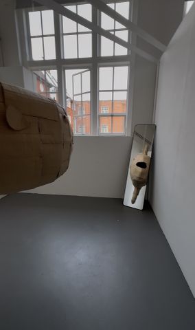 A large cardboard sculpture hanging from ceiling with a mirror reflection.