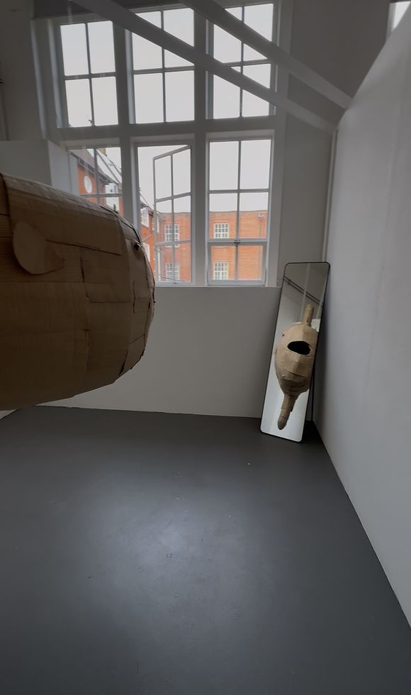 A large cardboard sculpture hanging from ceiling with a mirror reflection.