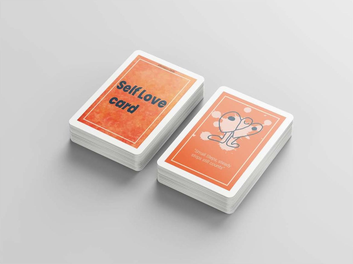 Photo of two decks of cards, one with "Self Love Card" on orange background on top, the other with blotches over stick person and message "Small steps, steady steps, still counts" on top