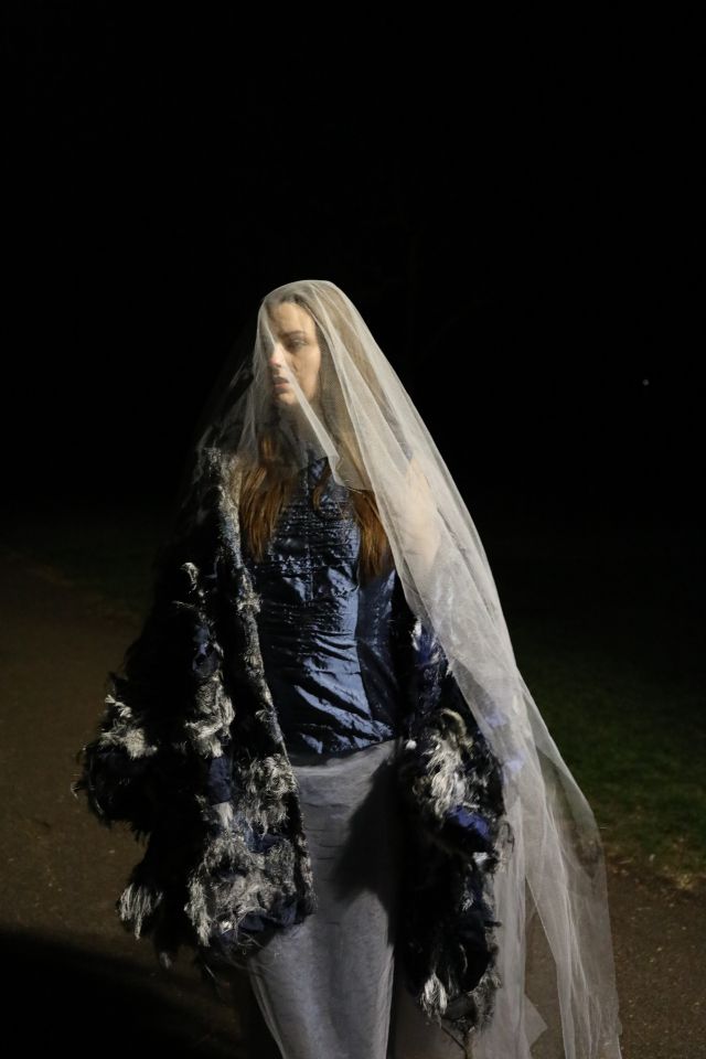Photo of female model wearing silvery blue coat, blue top, grey skirt and white veil