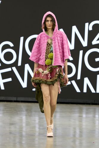 Female model wearing brown spotty top, red and green short skirt and pink hooded blouse on GFW2026 catwalking sides on GFW2026 catwalk