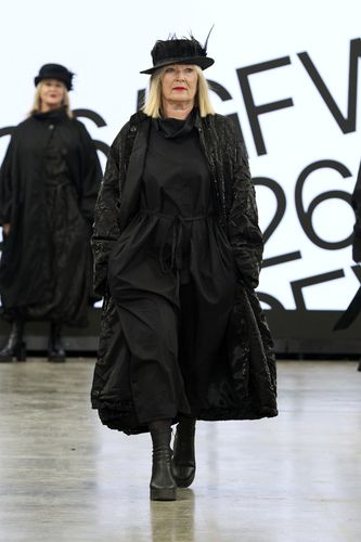 Mature female model wearing all black outfit and hat on GFW2026 catwalk