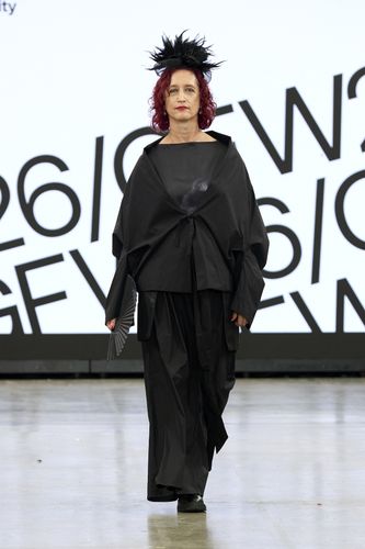 Mature female model wearing all black outfit and hat on GFW2026 catwalk