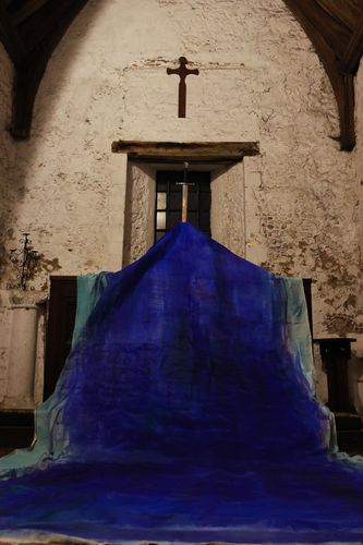 Fine Art display of blue material in front of window beneath cross