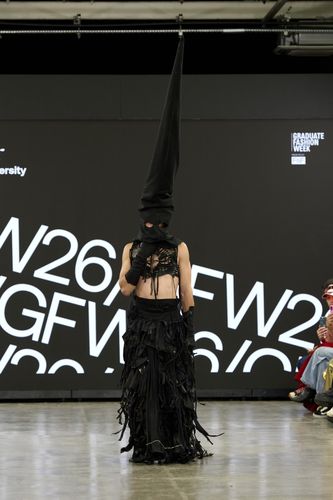 Male model wearing black skirt, gloves, short top and long black conical hat on GFW2026 catwalk