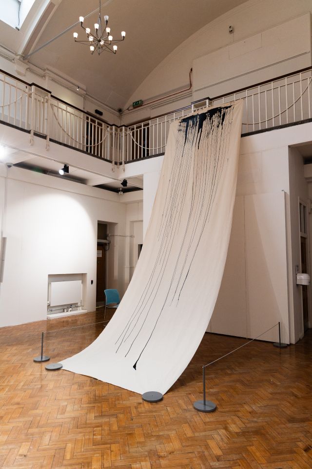 Fine art piece with large sheet of paper running with black paint dribbles