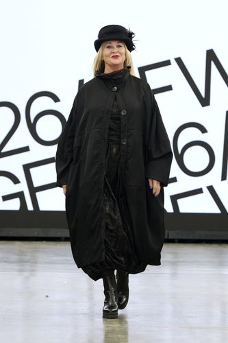 Mature female model wearing all black outfit and hat on GFW2026 catwalk