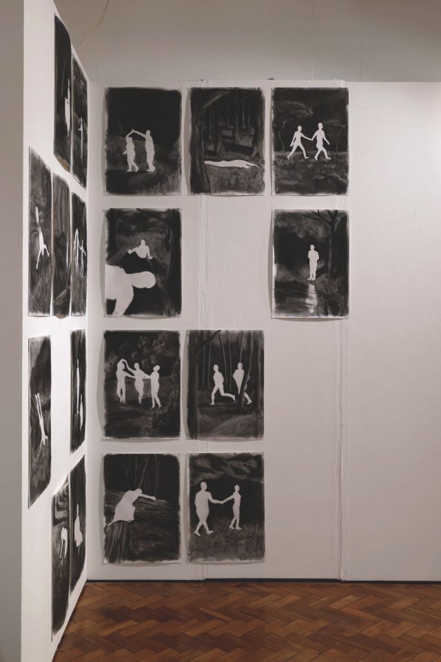 Many negative charcoal images of people in different poses on gallery wall