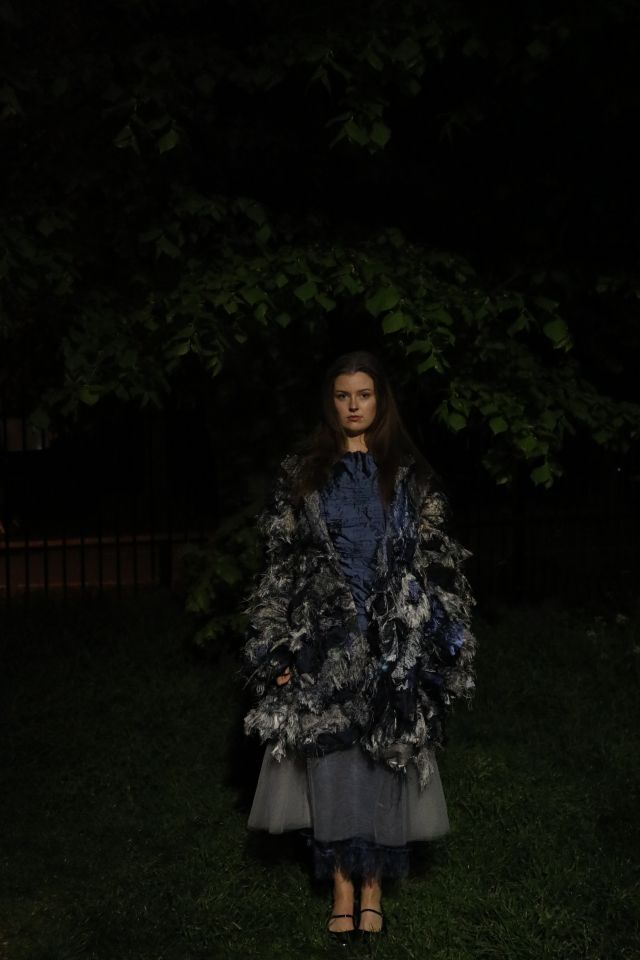 Photo of female model wearing silver blue coat, grey skirt and blue top in front of tree at night