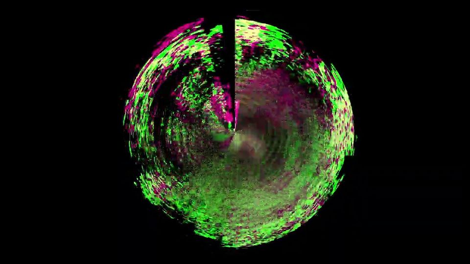 Video frame showing circle comprised of green and purple speckles