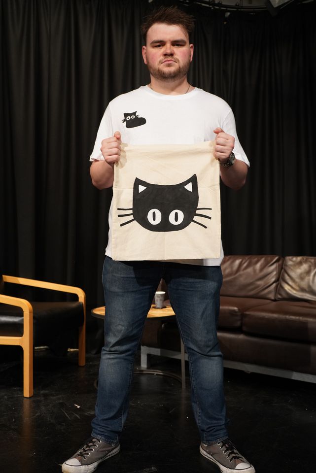Man holding white bag with black cat and wearing white t-shirt with black cat