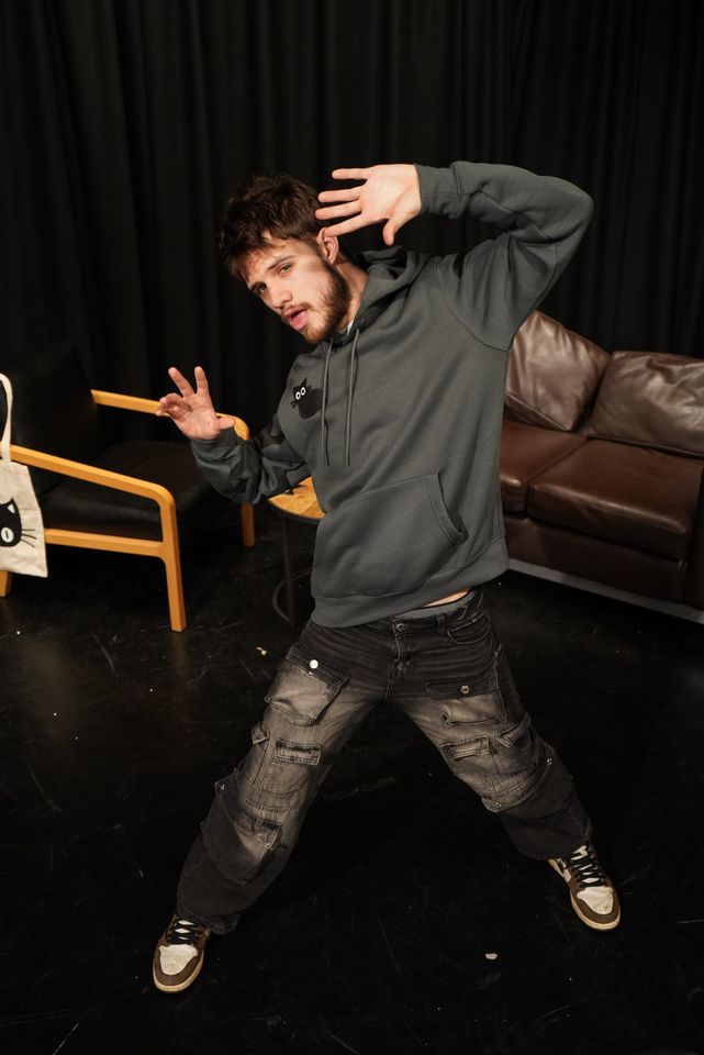 Man striking pose while wearing grey hoodie with black cat on chest