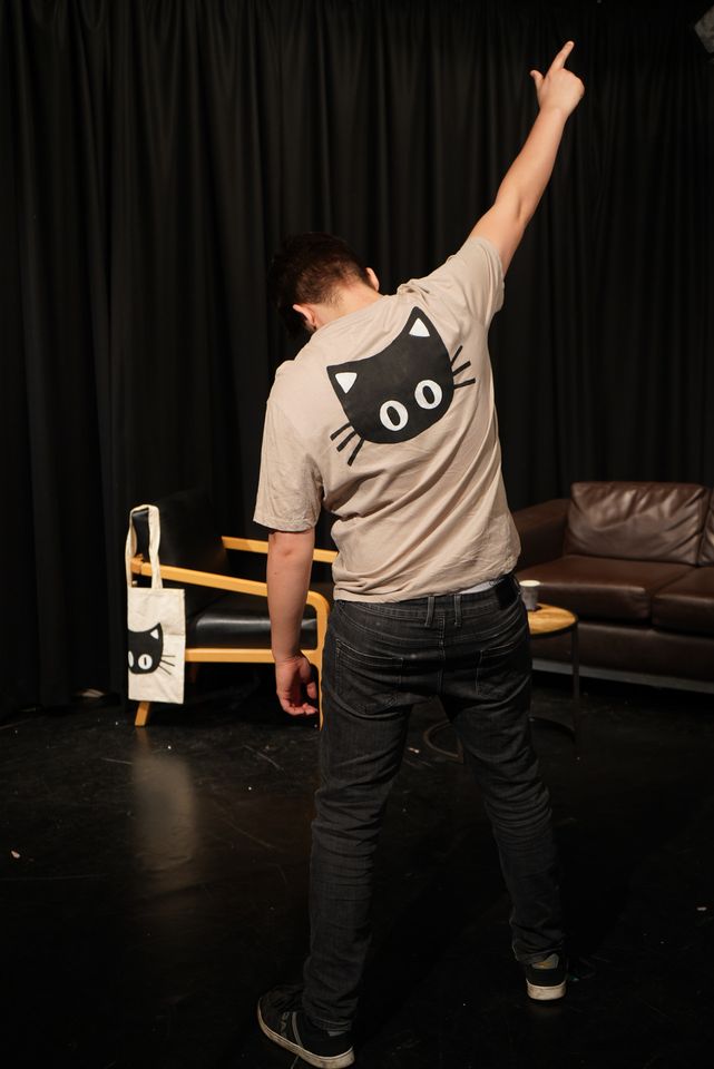 Man with back to camera wearing beige t-shirt with big black cat face on back