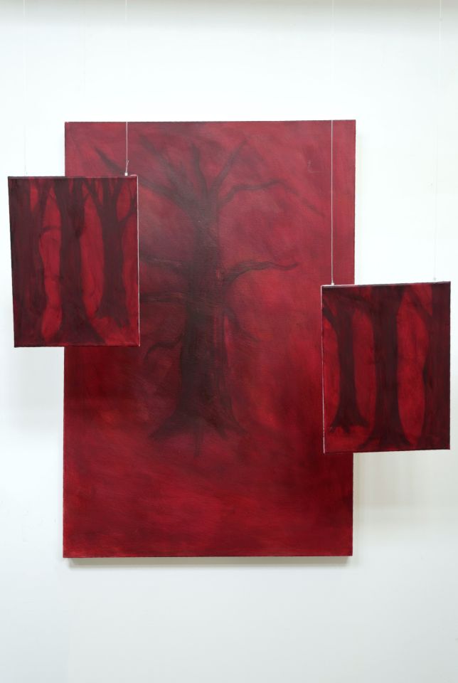 Image of tree with deep red background on wall with two smaller similar images of trees suspended in front of it