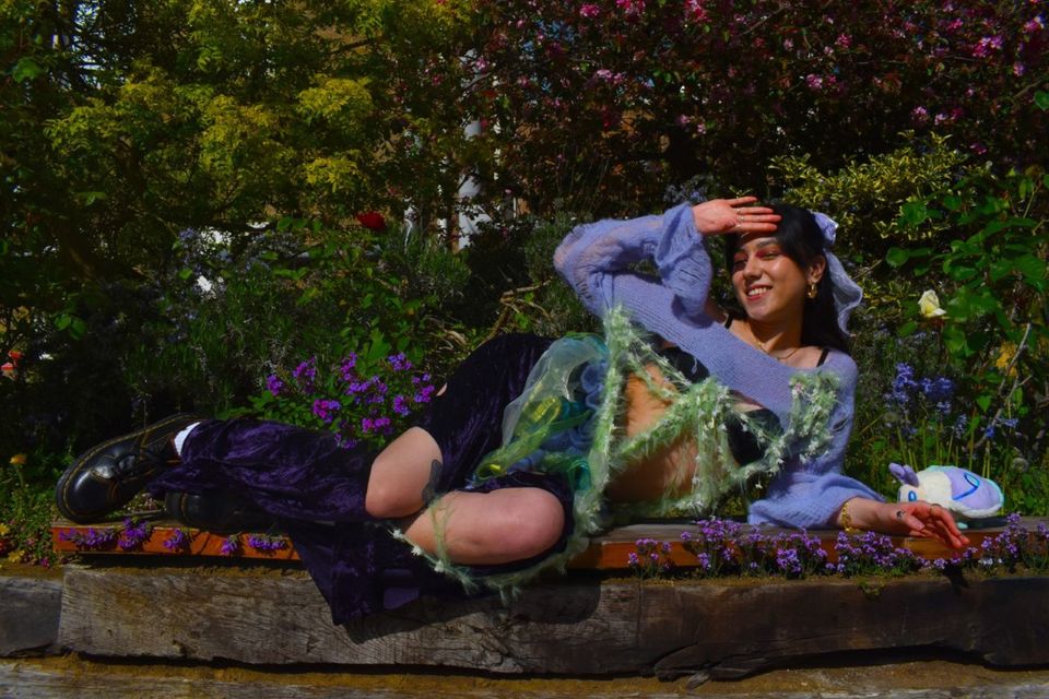 Photo of female model lying on garden wall wearing purple, green and black outfit