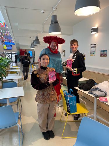 Three people in colorful costumes holding flyers for Cinderella, standing in the Street, Helmore Building, on ARU Cambridge campus