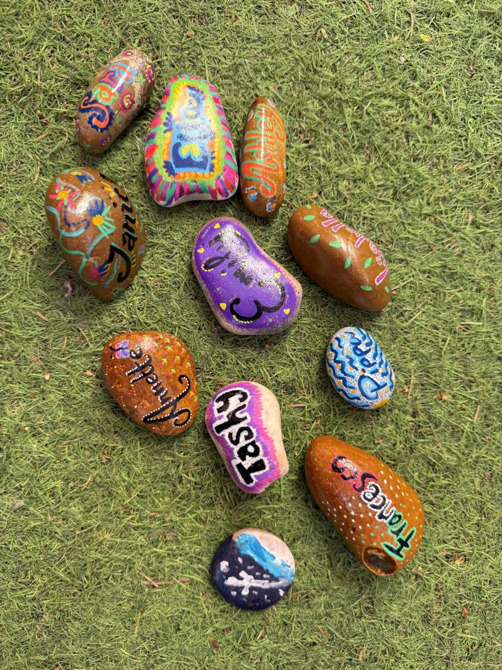 Colorful painted rocks with words like "laugh" and "thankful," arranged in a heart shape on grass.