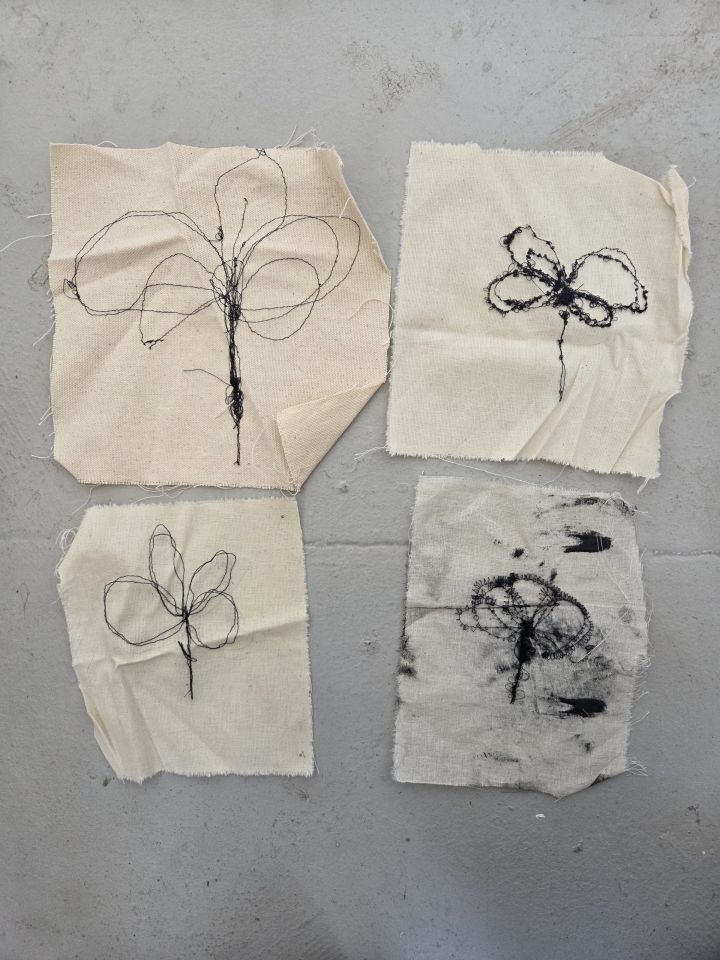 Four pieces of cloth with flowers stitched into them with black thread