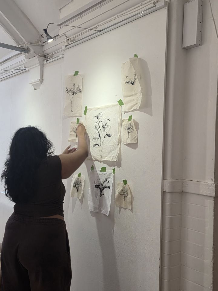 A person placing pieces of material with black plant-like designs on gallery wall